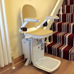 A reconditioned Acorn or Brooks 180 Curved Stairlift with a beige chair, armrests, and footrest is installed at the bottom of a striped carpeted staircase in a home, ready for use.