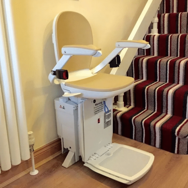 A reconditioned Acorn or Brooks 180 Curved Stairlift with a beige chair, armrests, and footrest is installed at the bottom of a striped carpeted staircase in a home, ready for use.