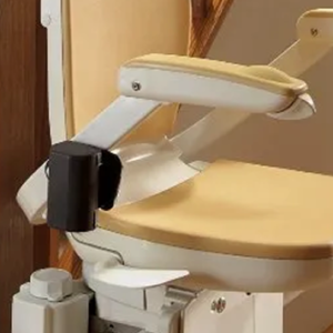 The T565 Brooks 180 Curved Stairlift - New, featuring a beige chair with armrests and backrest, is installed along a curved staircase with wooden bannisters and flooring to assist people with mobility issues in moving between floors.